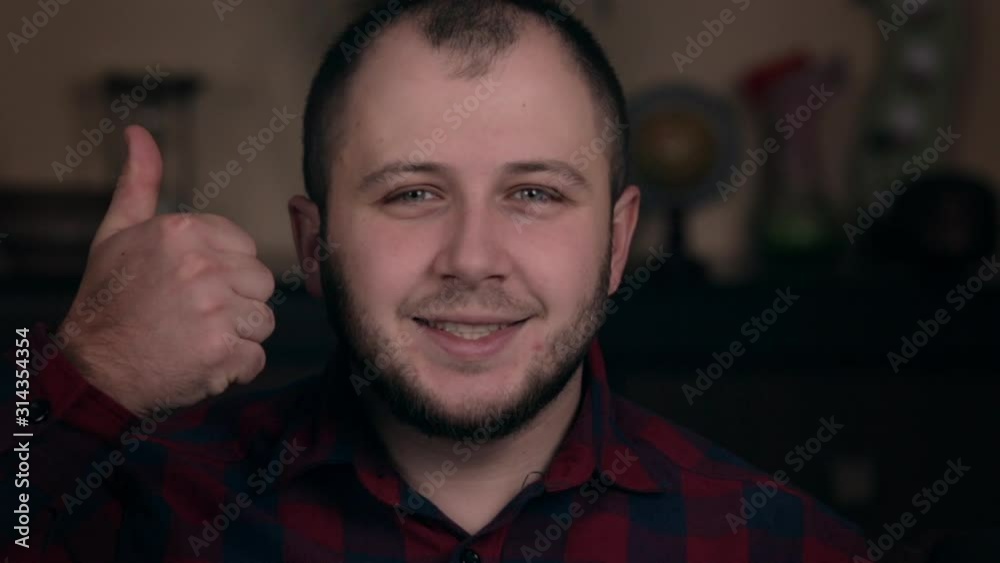 A young guy of European appearance sits in a chair in a plaid shirt shows a like and respect into camera A young guy of European appearance sits in a chair in a plaid shirt shows a like and respect into camera