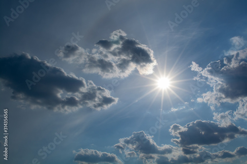 Sun with rays on a background of blue sky with clouds