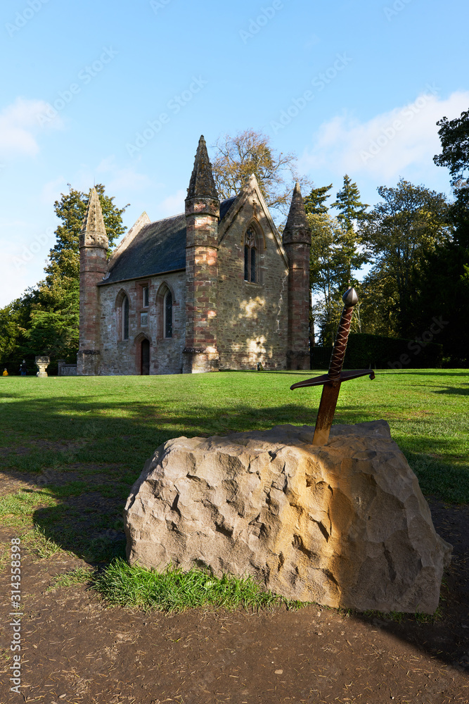 Old sword sticking in a stone on green gras in front of a church in Scotland