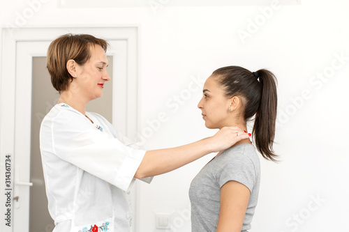 young woman professional short-haired therapist in a bright medical office, examines a patient, feels the thyroid gland