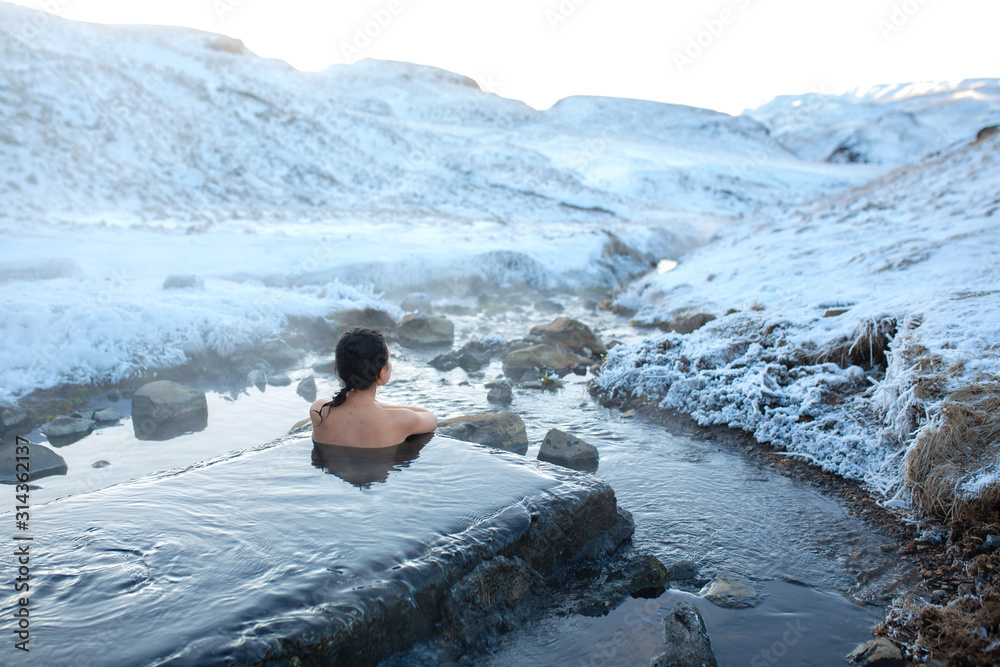 The girl bathes in a hot spring in the open air with a gorgeous view of the snowy mountains. Incredible iceland in winter - obrazy, fototapety, plakaty 