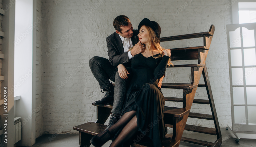 Romantic couple sitting on wooden steps. Man and woman in stylish hats and sweaters. Vintage english style Romantic couple sitting on wooden steps. Man and woman in stylish hats and sweaters. Vintage english style