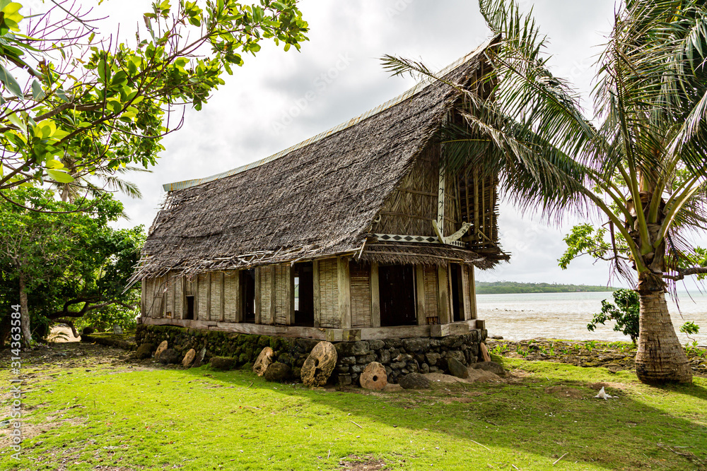 Obraz premium Old traditional thatched yapese men's meeting house faluw or fale, on an elevated limestone platform with bank of rai stone money. Shore of South Pacific ocean. Yap island, Micronesia, Oceania