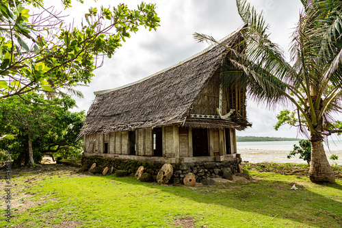 Old traditional thatched yapese men's meeting house faluw or fale, on an elevated limestone platform with bank of rai stone money. Shore of South Pacific ocean. Yap island, Micronesia, Oceania