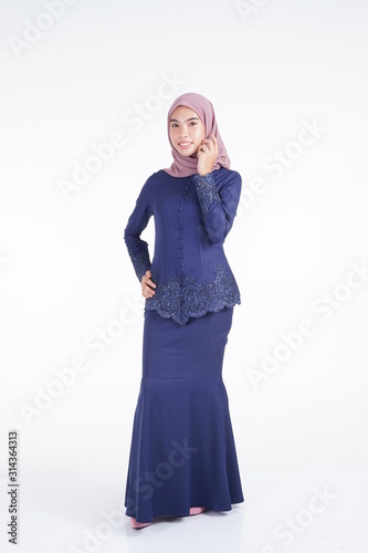 A beautiful Muslim female model wearing a dark blue modern kebaya with hijab, an Asian Muslim traditional dress isolated on white background. Eidul fitri fashion and lifestyle portrait concept.