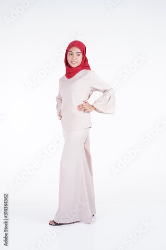 Attractive Muslim female model wearing a cream colored modern kebaya with red hijab, an Asian Muslim traditional dress isolated on white background. Eidul fitri fashion and lifestyle portrait concept.