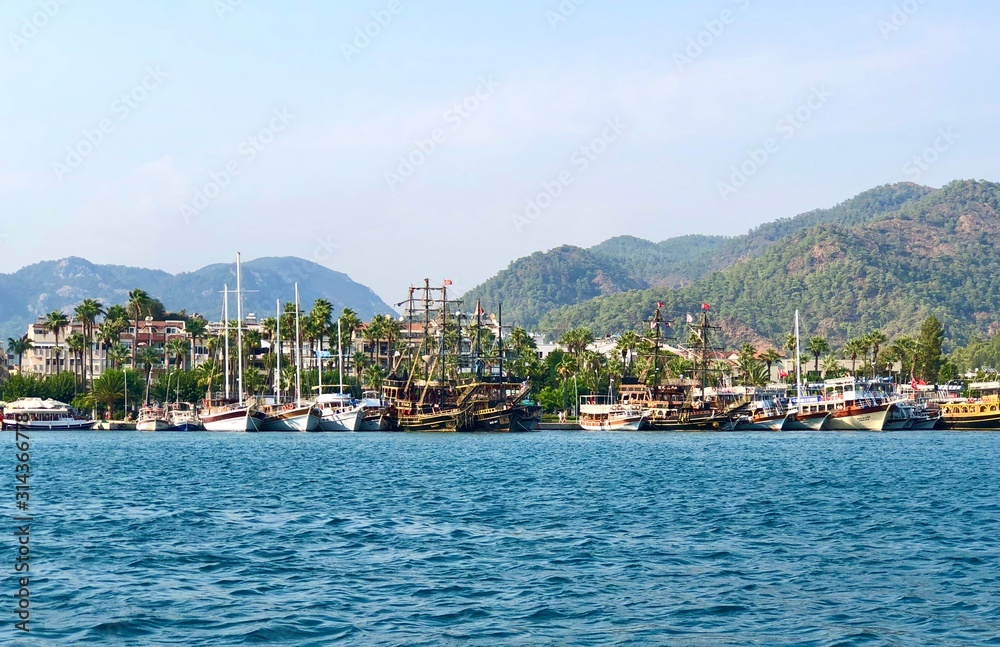 Beautiful seascape, view from boat. Sea coastline with parked yachts and ships. mountains covered with green trees on the horizon, bright blue sky on a sunny day