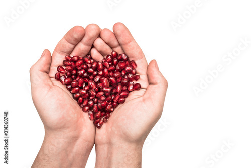 A man holds a heart made of ripe pomegranate seeds in his hands. Care of the heart and love. © Availaisu
