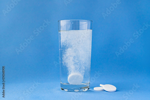 Fizzy aspirin in a glass of water on a blue background. Vertical format and soft focus. photo