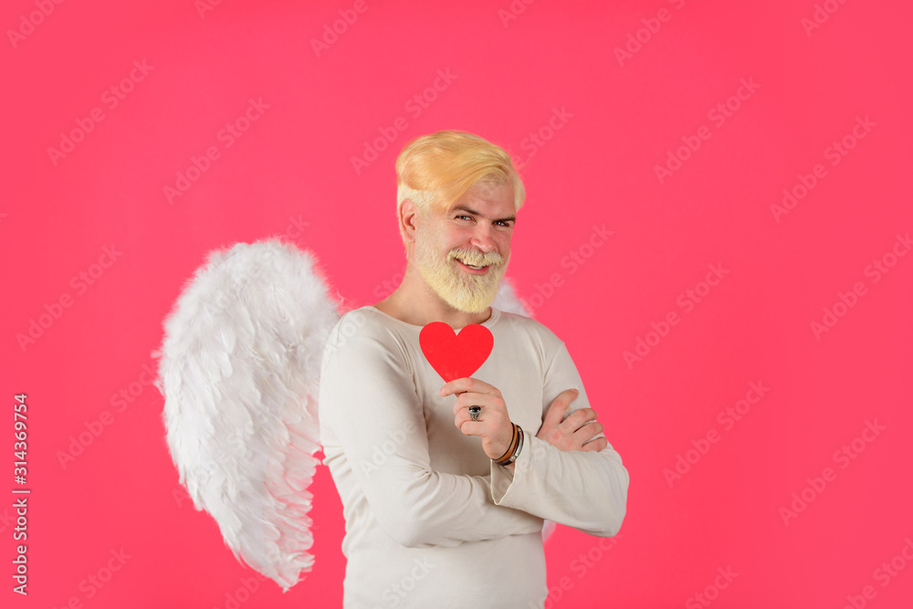 Obraz premium Cupid in valentine day. Male angel with red heart. Bearded man with angel wings holds paper heart. Blonde cupid with white angel wings. Happy Valentine Day. Cupid. Amour. Valentine cupid. February 14.
