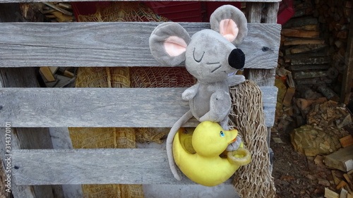 The soft toy rat rides on a yellow rubber duck inserted into a wall of firewood shed