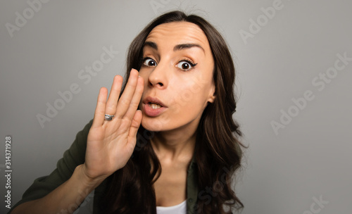 Let me tell you something. Close-up photo of a gorgeous girl with long chestnut hair, who whispers something to the camera.
