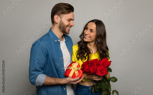 Lovely box. Close-up photo of a handsome man, who is giving a present and a bouquet of red roses to his girlfriend, while looking into her happy eyes.