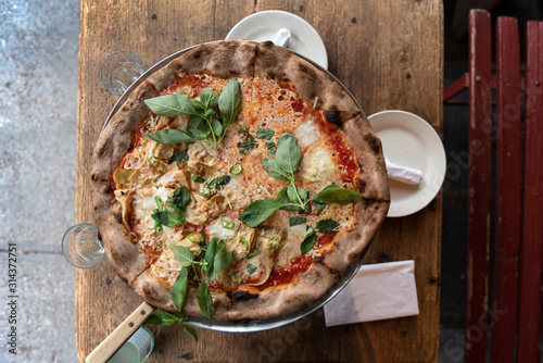Whole pizza with  basil, artichokes, japalenos and cheese on a restaurant table