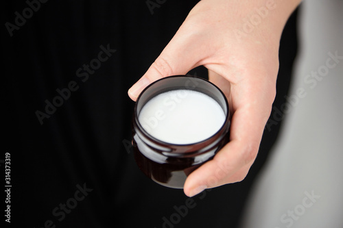 Shea butter in jar, cosmetic product for moisturizing skin. Female hand holds container with white anti-aging smoothing and soothing cream
