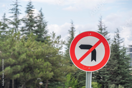 Traffic Sign Do not turn Left with blur background oh pine tree and cloudy sky