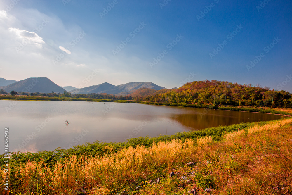 The blurred panoramic nature background of sunlight hitting the lake's surface, grass and wind blowing all the time along the large mountains, ecological beauty and fresh air.