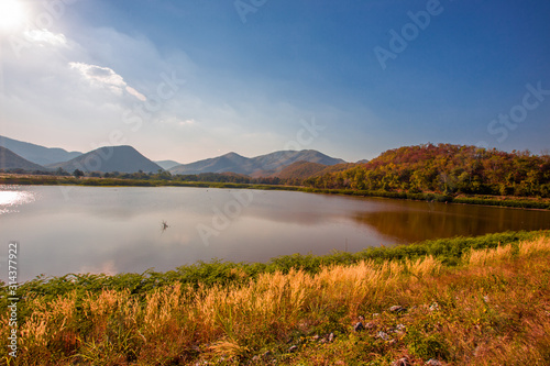 The blurred panoramic nature background of sunlight hitting the lake's surface, grass and wind blowing all the time along the large mountains, ecological beauty and fresh air.