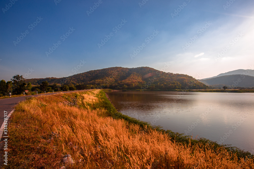 The blurred panoramic nature background of sunlight hitting the lake's surface, grass and wind blowing all the time along the large mountains, ecological beauty and fresh air.