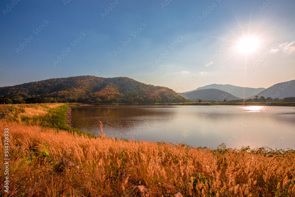 The blurred panoramic nature background of sunlight hitting the lake's surface, grass and wind blowing all the time along the large mountains, ecological beauty and fresh air.