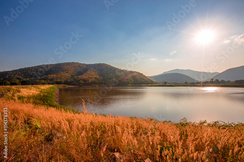 The blurred panoramic nature background of sunlight hitting the lake's surface, grass and wind blowing all the time along the large mountains, ecological beauty and fresh air. © bangprik