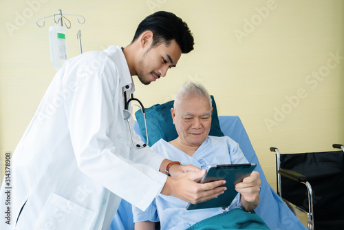 Asian man doctor uses a tablet to explain the treatment of senior male patients lying in hospital beds. Modern medical care Use technology to treat Concept of looking after elderly and retirees