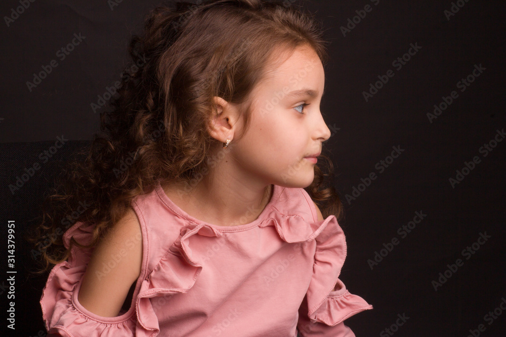 Studio portrait of little girl with long curly hair, in a pink skirt and black shorts, sitting on an office chair Studio portrait of little girl with long curly hair, in a pink skirt and black shorts, sitting on an office chair