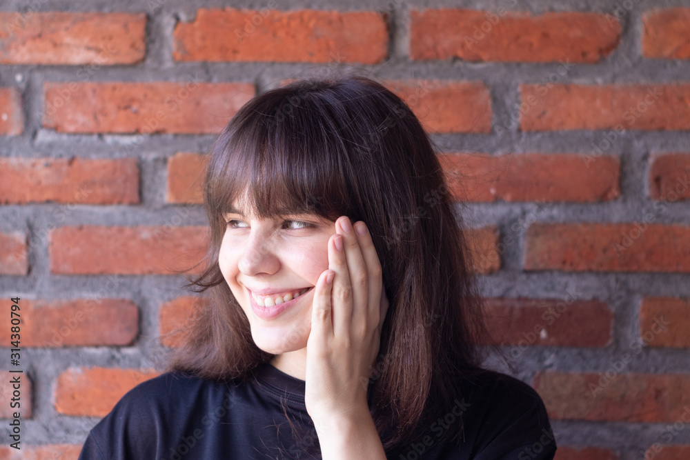Portrait of a beautiful brunette woman with bangs wearing a black t-shirt who is happy and smiling on brick wall background Portrait of a beautiful brunette woman with bangs wearing a black t-shirt who is happy and smiling on brick wall background