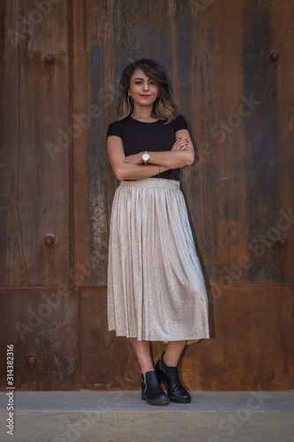 portrait of a beautiful latin woman with shirt, white skirt and folded arms in rusty iron background