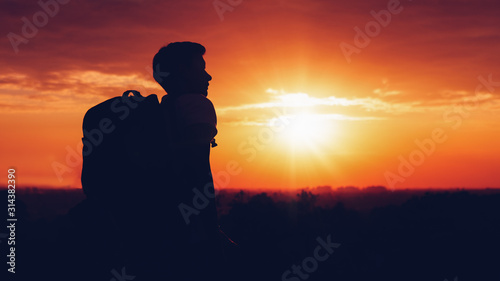 silhouette of man hiker standing on rocky mountain peak with sunset golden sky feeling of freedom