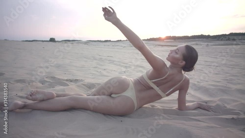 A beautiful dark hair dancer girl in a light bikini swimsuit dancing in the evening desert. Contemporary dance in the desert on the sand. Beautiful woman dancer in a swimsuit dancing.