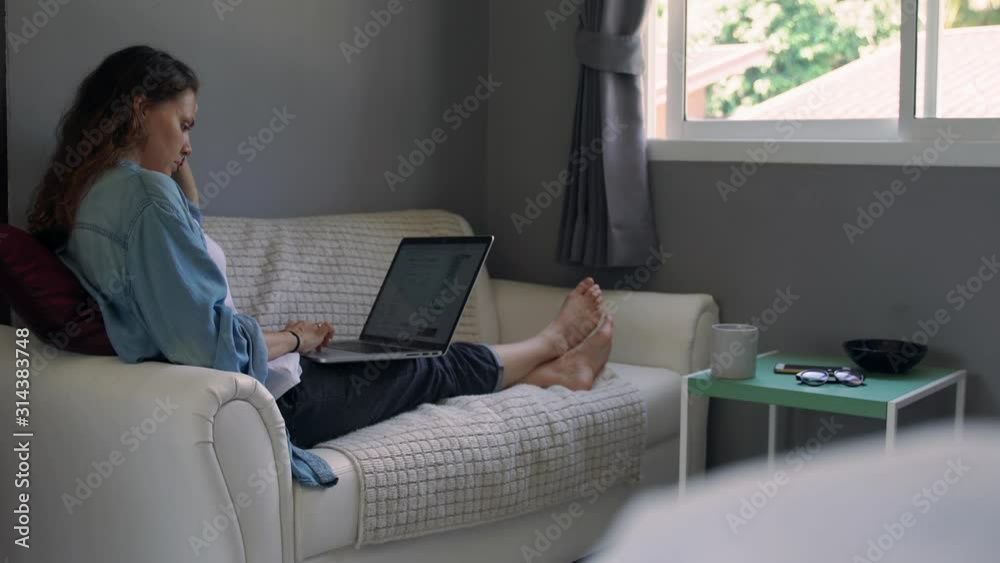 A young woman with a laptop sitting on the couch in the living room and searching for information on the internet. A young student preparing for the exams. A young woman with a laptop sitting on the couch in the living room and searching for information on the internet. A young student preparing for the exams.