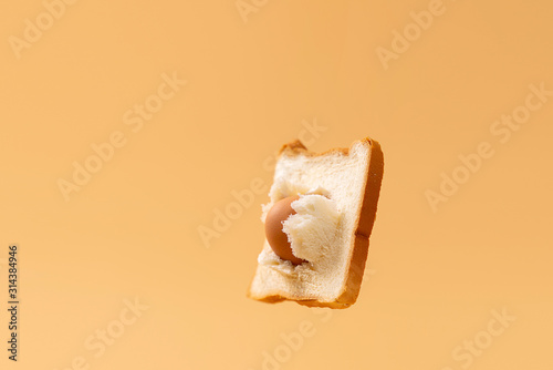 Suspended in front of a yellow background, an egg passes through the middle of a piece of toast.