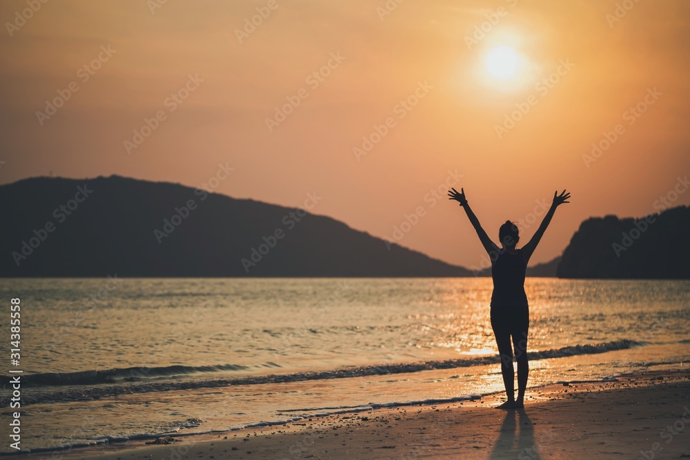 Asian women play yoga on a sand beach by the sea and mountain background in the sunrise morning. Exercise and meditation concept.