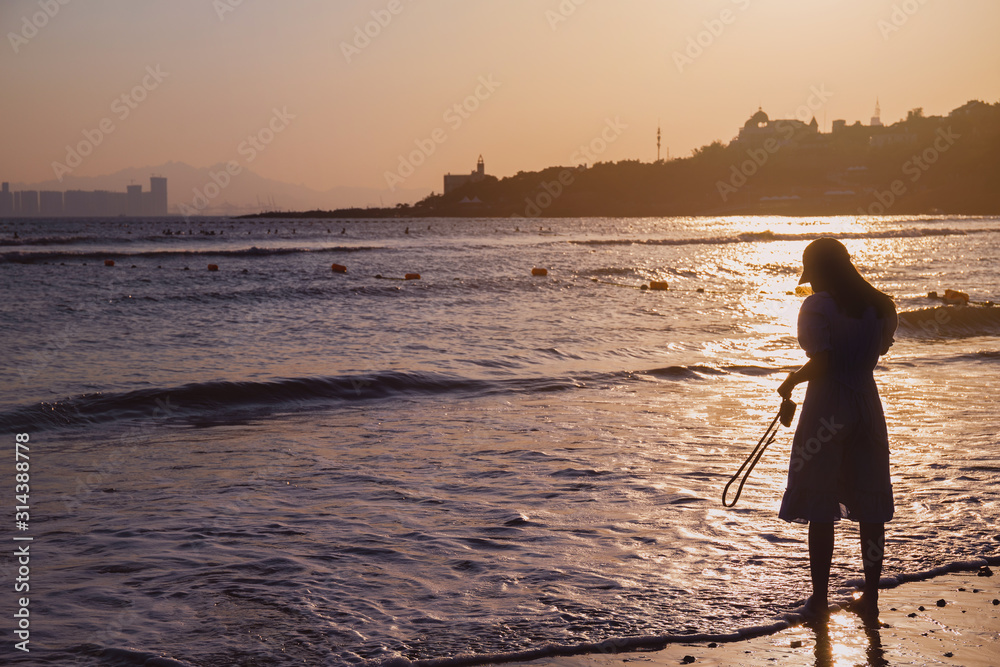 Silhouettes of Asian traveller woman standing on the beach in sunset background with vintage filter