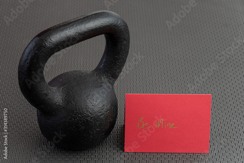 Holiday fitness, black kettlebell, with a red valentine card, on a black gym floor