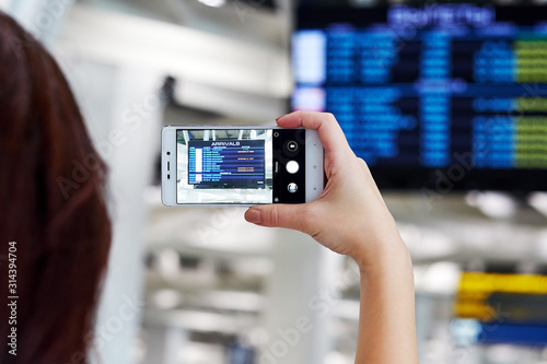 Hand takes photo on smartphone in airport. On the screen, the flight departure schedule