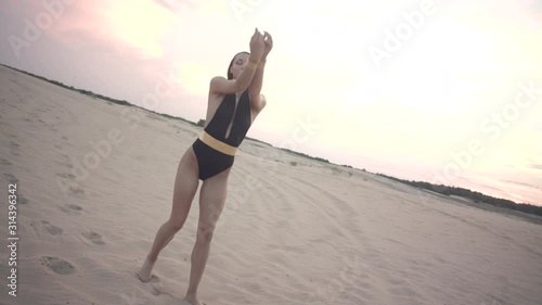 Portrait of dancer young dark-haired woman wearing black swim bodysuit in the desert. Portrait of a young fashion model in sunset light.
