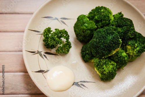steamed broccoli with mayonnaise on the brown plate and the wooden background   