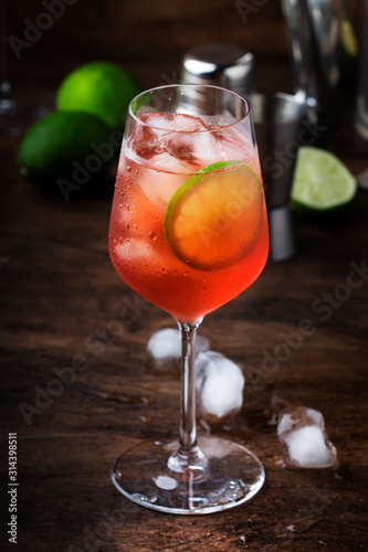 Campari tonic alcohol cocktail with red bitter, tonic, lime and ice. Old wooden table background, bar tools, selective focus. Copy space