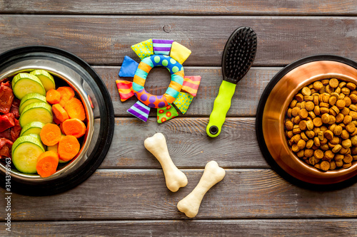 Dog feed - dry food and raw meat - near toy, brush and cheving bones ondark wooden background top view photo