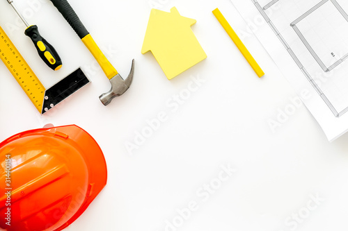 Construction concept. Helmet, tools on work desk, house cutout on white background top-down frame copy space