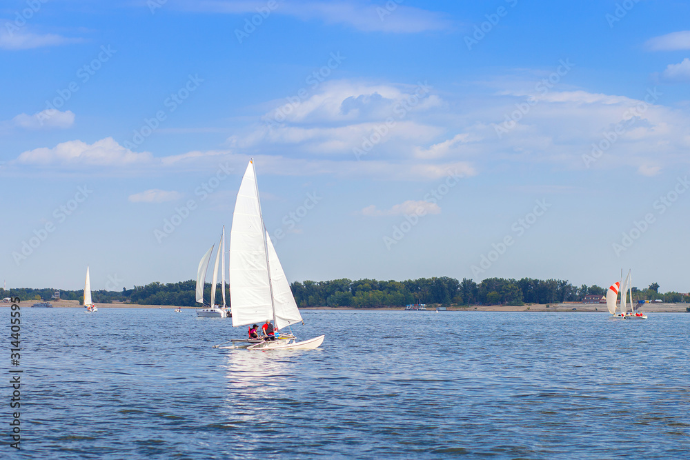A yacht with a white sail floats on the river as part of a sailing regatta