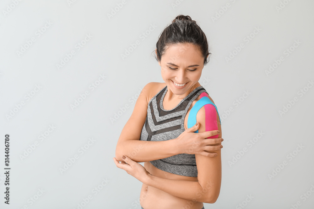 Sporty woman with physio tape applied on shoulder against light background Sporty woman with physio tape applied on shoulder against light background