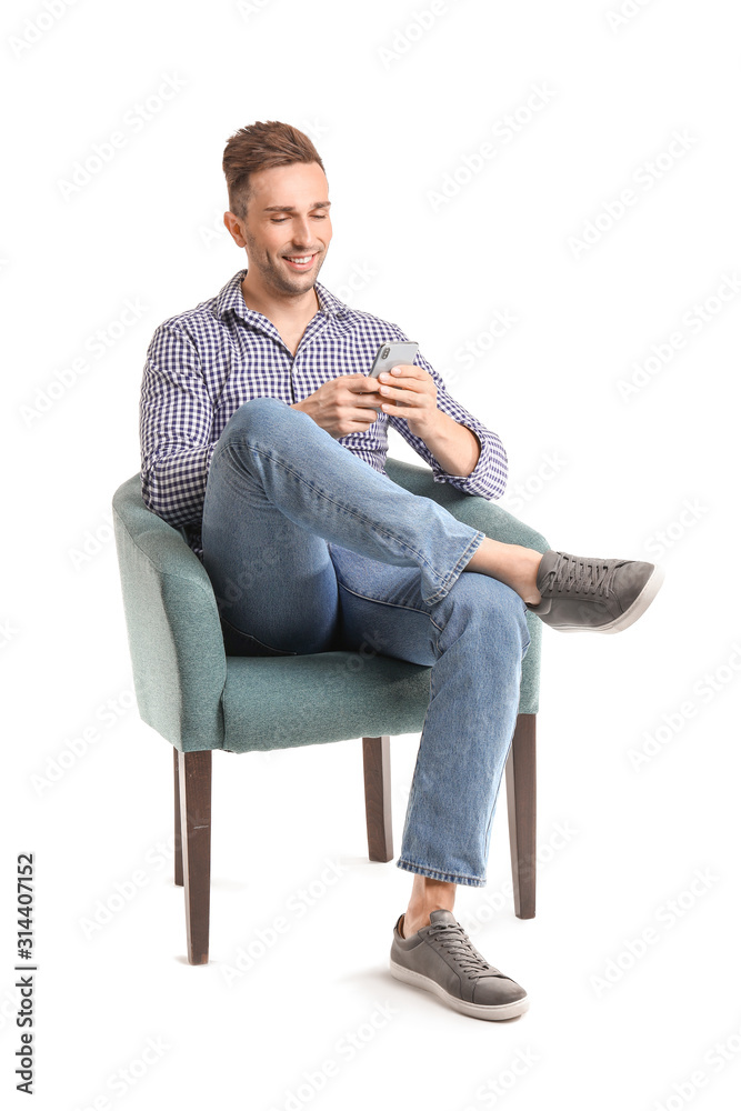 Handsome man with mobile phone sitting in armchair on white background