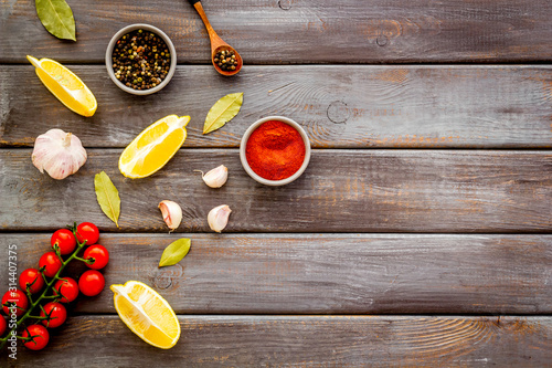Cooking background with spices - pepper, garlic, cherry tomatoes - on dark wooden desk top-down frame copy space