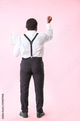 African-American teacher writing something on color background