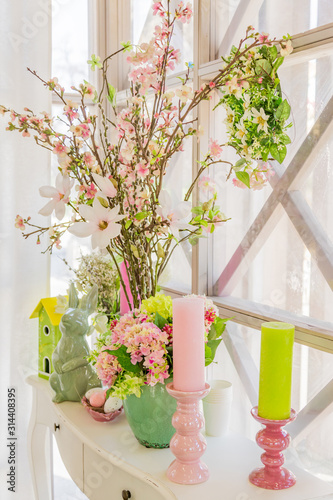 Easter interior decoration. Beatuful composition with candles. eggs, rabbit, birds house and blooming apple branches.