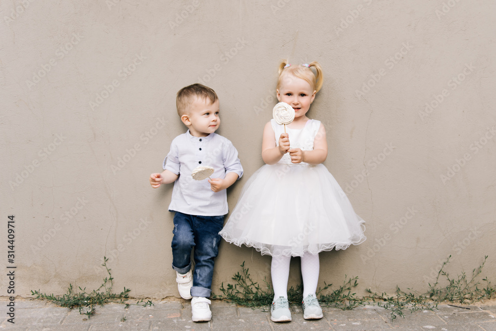 Stylish little boy and girl on a gray background with candy meringues in their hands