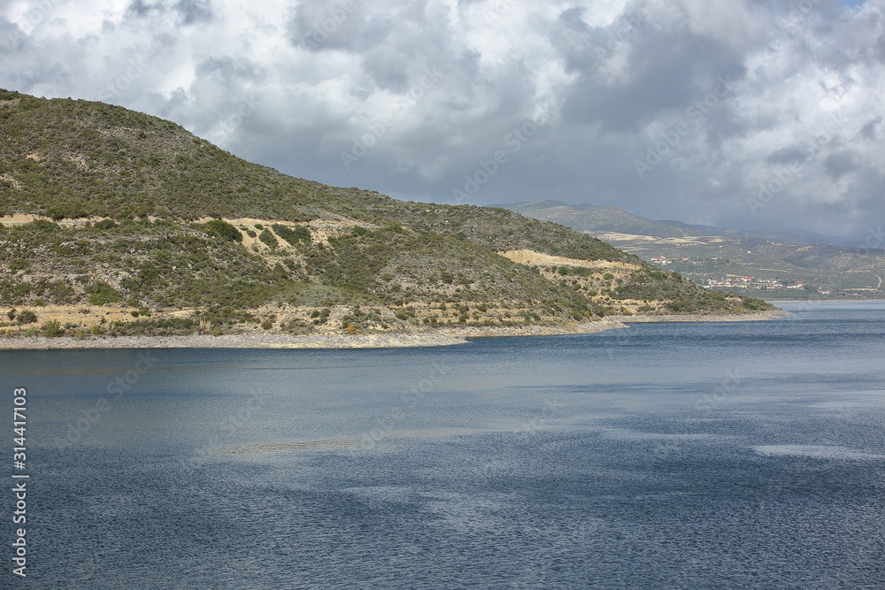 Lake surround with hills covered by rare arid plants, swirling rainy clouds over it